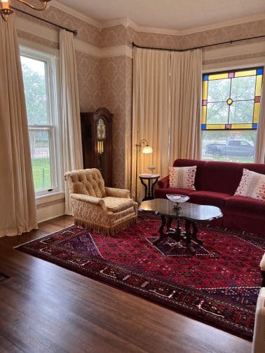 the front parlor in the Milton Parker Home in Bryan Texas with antique furnishings, a couch, lounge chair, windows and rug