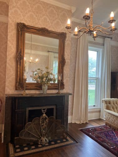 an antique fireplace, mirror, and chandelier in the parlor room at the Milton Parker Home in Bryan, Texas