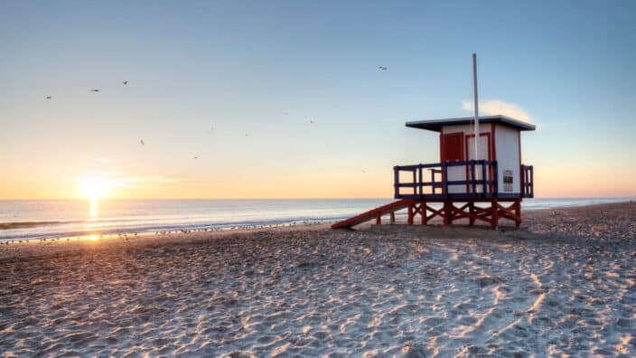 a red and white lifeguard stand on cocoa beach during sunset