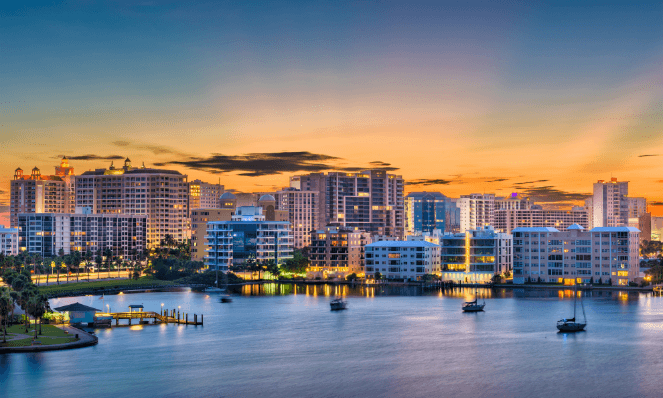 aerial view of a town in Florida during sunset with lit up buildings, glowing skies, and water to represent a Florida for Vacation getaway