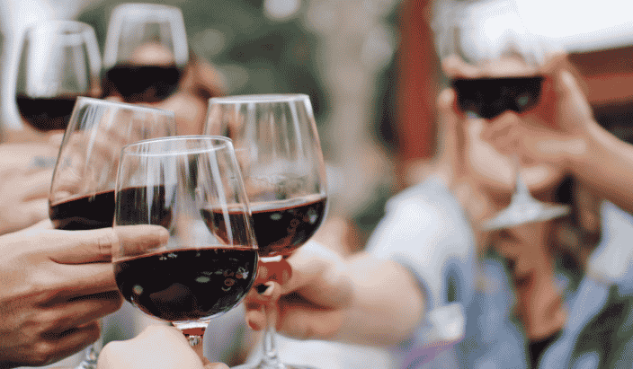 a group of people holding wine glasses with red wine and toasting each other