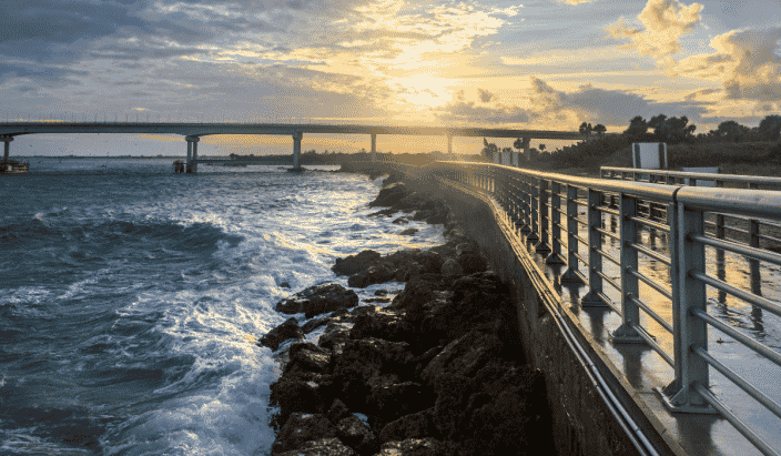 The Sebastian Inlet State Park at Vero Beach Florida with a long bridge, and water crashing against the rocks along the side of the bridge with golden and cloudy skies