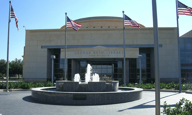 the George H. Bush Presidential Library with blue skies, a fountain, and flags out in front of it 