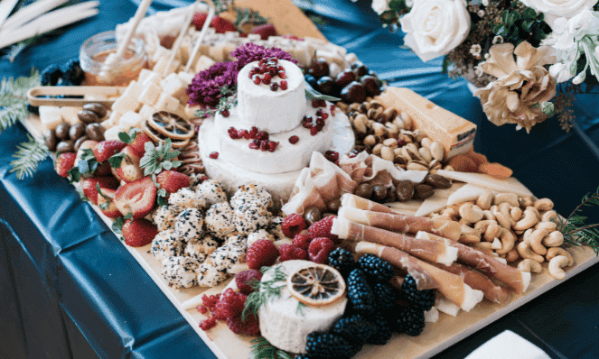 a close-up of an elaborate charcuterie board with goat cheese, cured meats, nuts, flowers, and fruits for summertime entertaining
