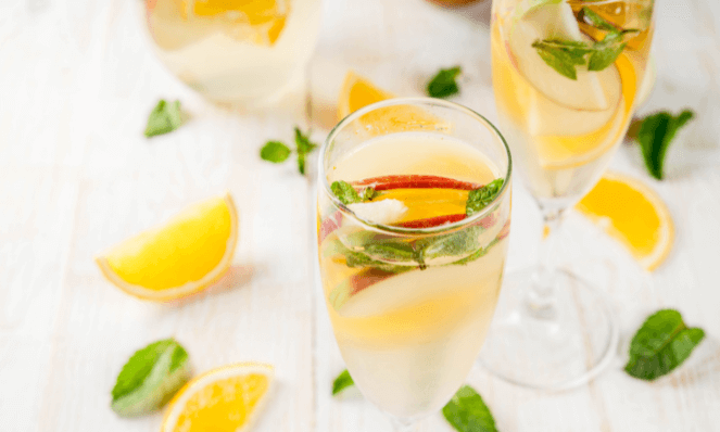 white citrus sangria in champagne glasses on a white wooden background with sliced oranges and mint