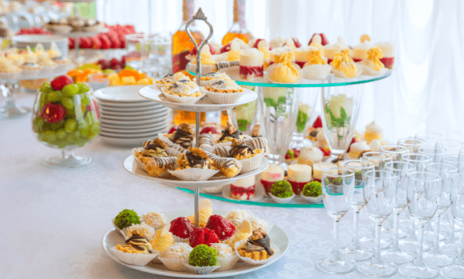 a table with pastry stands on it with small pastries, fruits, champagne glasses, and plates for summertime entertaining 