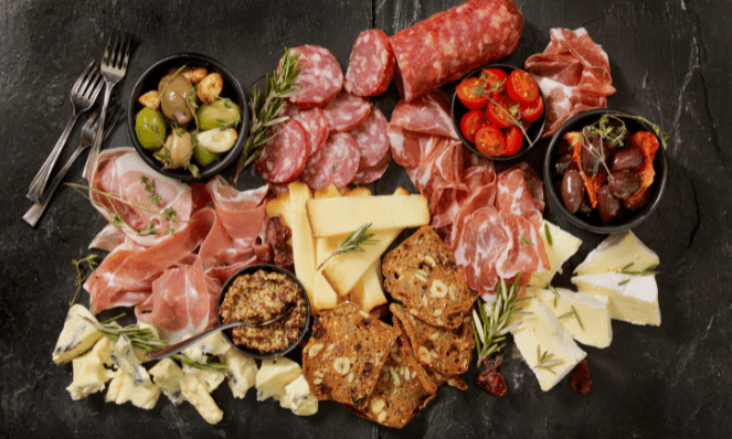 a slate board with an assortment of cured meats, cheeses, crackers, and spreads on it to make a charcuterie board