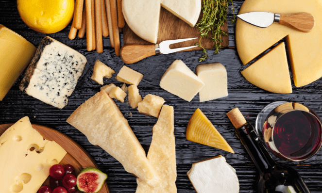 various cheeses, cheese tools, fruits, bread sticks, and wine bottle with cork. These are the essentials for a cheese and wine pairing