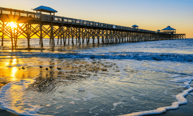the pier at folly beach with the sun setting, golden skies and blue water
