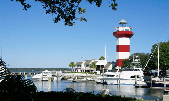 hilton head island with a red and white lighthouse, yachts docked at the harbor and blue skies