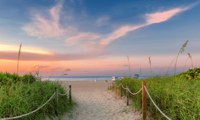 a beach at sunset with pink and blue skies and sea grass on either side of the walkway representing romantic beach getaways in the south