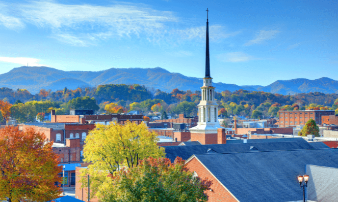 Johnson City, Tennessee with blue skies, a steeple, trees with orange and green leaves and mountains in the background, the perfect place for Tennessee romantic getaways