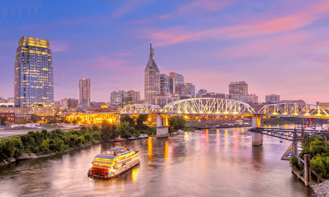 nashville, tennessee at sunset with pink and purple skies, a bridge, river, and river boat with high rise buildings in the background