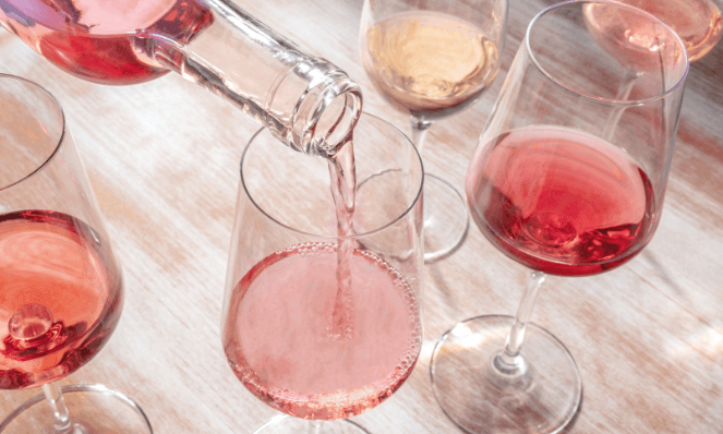 multiple glasses of rose on a wooden table with a bottle filling up another glass for cheese and wine pairing