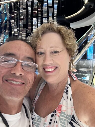 Jim and Betsi Hill on a ship with a gleaming silver and glitter stairway behind them