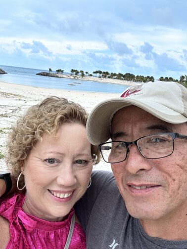 Betsi Hill and Jim Hill of Betsi Hill Travel and BetsiWorld on beach with water and trees in the background