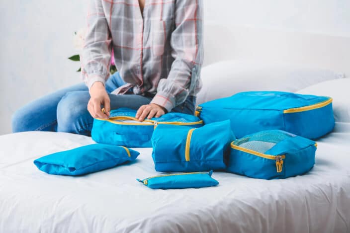 Traveler organizing blue packing cubes filled with winter clothing, showing efficient packing for cold weather holiday trips and seasonal travel.