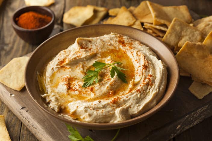 a bowl of hummus with a sprig of parsley on top